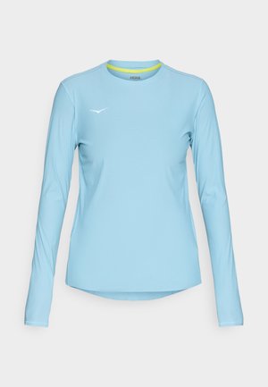 Chemise à manches longues bleu clair en tissu respirant, dotée d'un col rond avec un accent jaune et d'un petit logo blanc sur la poitrine.