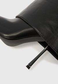 Čierna kožená členková čižma s elegantným dizajnom, vybavená špicatou špičkou a podpätkom ihličkového tvaru. Textúra je hladká s jemnými švami.