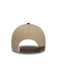 Μπεζ καπέλο από καμβά με στρογγυλεμένο στέμμα, καφέ δερμάτινο λουράκι και ορειχάλκινα υλικά. Διαθέτει ραμμένο πάνω κουμπί και ετικέτα με λογότυπο.