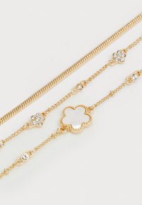 Gold-tone jewelry featuring a snake chain and two delicate chains with floral accents and clear gemstones, creating elegant detailing.