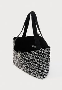 Čierno-biela plátená taška s geometrickým vzorom a detailom loga, vybavená dvoma pevným rukoväťami a otvoreným horným okrajom pre jednoduchý prístup.