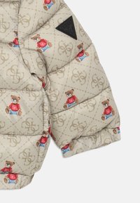 Beige quiltet jakkeerm med ermer prydet med teddy-bjørner iført røde skjorter og blå jeans, med et svart GUESS trekantet logo-merke.