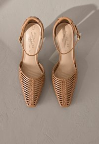 Zapatos slingback de cuero marrón con detalles trenzados, punta afilada, correa en el tobillo con un hebilla dorada y un forro interior suave.