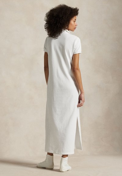 Valkoinen, polvenpituinen mekko, joka on valmistettu pehmeästä, teksturoidusta kankaasta. Siinä on kaulus, lyhyet hihat ja sivuhalkiot liikkuvuuden helpottamiseksi.