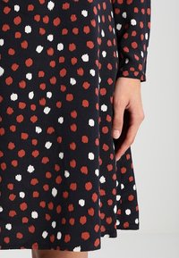 Mekko, jossa on tummansininen tausta, jossa on kuvio punaisista ja valkoisista pisteistä. Kangas näyttää pehmeältä, ja siinä on kevyesti teksturoitu pinta.