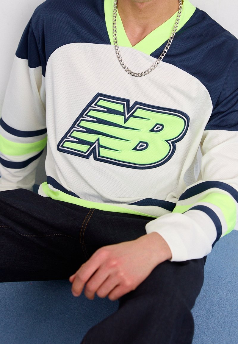 Weißes und marineblaues Jersey mit neongrünen Akzenten, ausgestattet mit einem großen Logo. Mesh-Struktur, lange Ärmel und kontrastierende gestreifte Details.