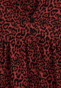 Sarkans un melns leopardu raksts audums ar pogu slēgtu plāksni augšdaļā un uzkrātu svārku detaļu, demonstrējot teksturētu rakstu.