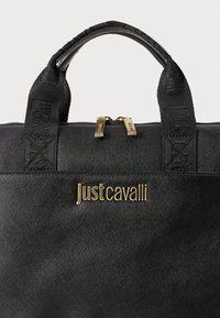 Juoda tote rankinė su tekstūruotu audiniu, dviguba auksinės spalvos užtrauktukų sistema ir įspaustas logotipas. Yra patvarūs dvigubi rankenai ir raštuoti diržų akcentai.