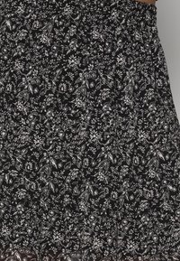 Tissu noir avec un motif dense de fleurs blanches et de feuilles, comportant de petites fleurs et des branches, rassemblé à la taille par un élastique.