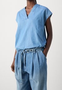Lyseblå denimtop med V-udskæring og korte ærmer, parret med højtaljede, plisserede matchende denimbukser. Teksturstof.