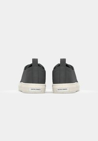 Bottines grises à enfiler avec un dessus texturé, semelle blanche contrastante et languettes à l'arrière. Étiquette de marque visible sur le côté.