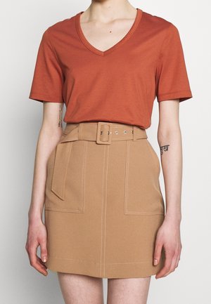 Person wearing rust-colored V-neck short sleeve top tucked into high-waisted beige skirt with a belt and front patch pockets.