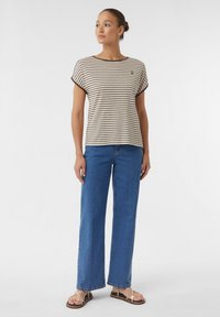 Gestreiftes kurzärmliges Top in Beige und Braun, kombiniert mit hochgeschnittenen, weiten blauen Jeans. Sandalen mit dünnen Riemen.