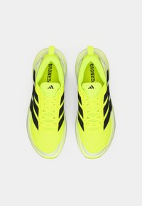 Bright yellow athletic shoes with black stripes, featuring a sleek design, mesh material, and a cushioned sole. Laces are yellow.