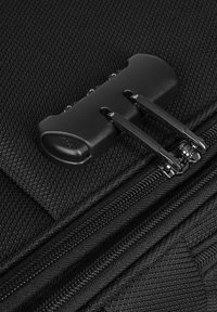 Dettaglio di una borsa in tessuto nero con superficie texturizzata, doppie cerniere metalliche e un manico per cerniera nero opaco.