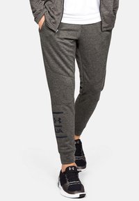 Grijze sportieve joggers van zacht materiaal, met een slim fit, zijzakken en een marineblauw Under Armour-logo langs het linkerpijp.