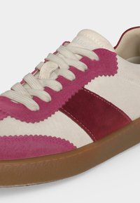 Λευκό και ροζ σουέντ αθλητικό παπούτσι με λαστιχένια σόλα, λευκά κορδόνια και διακοσμητικό ζιγκ-ζαγκ ραφτό κατά μήκος των ροζ πάνελ.