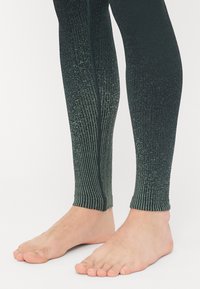 Leggings med svart-til-grønn gradient, vertikal ribbet tekstur og en glatt finish, med en tettsittende passform rundt anklene og uten synlige sømmer.