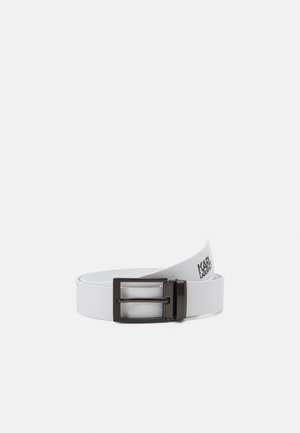 Witte leren riem met rechthoekige zwarte metalen gesp, deels opgerold, met het "Karl Lagerfeld"-logo aan de binnenkant.