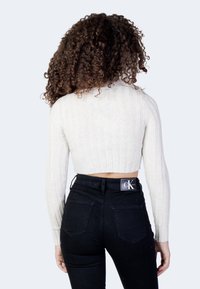 Maglione corto a coste crema con maniche lunghe, abbinato a jeans neri a vita alta con un logo sulla cintura.
