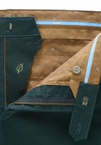 Donkergroene broek met open ritssluiting, die een bruine patroonvoering vertoont met een knoop en blauwe afwerking, kleine geborduurde blaadjesdecoratie op de stoffen flap.