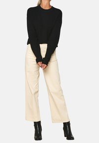 Musta pitkähihaine villapaita yhdistettynä kermaisiin leveälahkeisiin housuihin ja mustiin korkokenkäisiin nilkkabootseihin. Kangas näyttää sileältä ja pehmeältä.