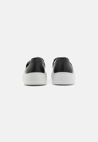 Zapatillas negras de cuero con una suela de goma blanca, con un diseño minimalista y una textura suave. La vista posterior resalta las líneas limpias y los acentos de costura.