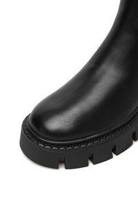 Czarne skórzane botki za kostkę z okrągłym noskiem, grubą fakturowaną podeszwą i dekoracyjnym przeszyciem wokół krawędzi. Stylowy, podwyższony design.