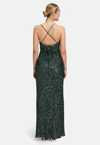 Langes grünes Paillettenkleid mit einer taillierten Silhouette, überkreuzten Trägern am Rücken und einem sanften Schleppe am Saum. Weiche Textur und Glanz.