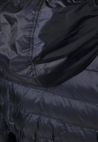 Svart puffjacka i material med en slät, glänsande yta som har horisontella sömmar och en samlad huva. Sömnadsdetaljer synliga.