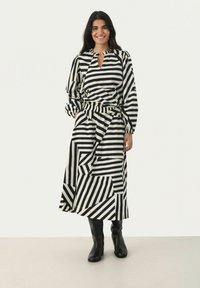 Robe à rayures noires et blanches avec des manches longues, décolleté en forme de clé, taille élastique et motifs géométriques alternés, assortie à des bottes noires hautes jusqu'aux genoux.