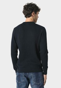 Maglione a coste blu navy con maniche lunghe, scollo rotondo e tessuto testurizzato. Indossato con jeans in denim, mostra una silhouette aderente dalla schiena.