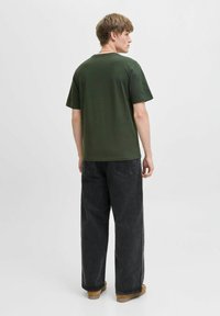 Camiseta de algodón verde de manga corta, con cuello redondo y corte relajado, combinada con jeans de pierna ancha negros y calzado marrón.