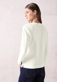 Lichtgroene geribde trui met een ronde halslijn en zijsplitten, gecombineerd met donkerblauwe jeans. Soepele textuur, casual pasvorm.