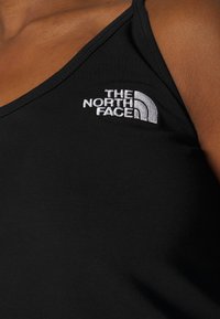 Top negro sin mangas hecho de una tela suave con un diseño de escote en V. Presenta el logotipo bordado en blanco de "The North Face" en el lado izquierdo.