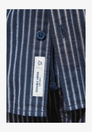 Marine gestreiftes Hemd mit blauen Knopf, featuring weiße vertikale Streifen und einem Etikett, das "DURABLE GOODS LOT. 002" liest. Glattes Material.