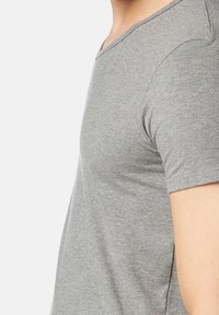 T-shirt grigio a maniche corte realizzato in tessuto morbido, con un design a V e una texture liscia, con cuciture visibili sulle spalle.