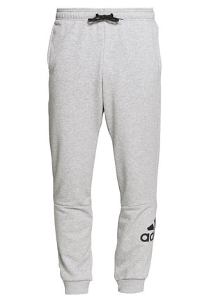 Jasnoszare spodnie dresowe ze czarnym sznurkiem, elastycznymi mankietami, bocznymi kieszeniami oraz czarnym logo Adidas na dolnej lewej nogawce.