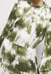 Groene en witte tie-dye jurk met lange, opgezette mouwen, gerimpelde halslijn en een sleutelgatdetail. Heeft een gelaagd rokontwerp.