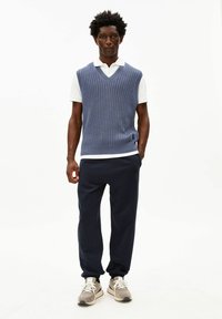 Blauw geribd gebreid vest over een wit overhemd met kraag, gecombineerd met marineblauwe joggers en grijze sneakers. Eenvoudig ontwerp zonder zichtbare patronen.