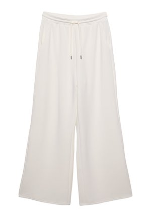 Pantalons amples de couleur crème en tissu doux, dotés d'une taille élastique, d'un cordon de serrage et de poches latérales. Texture lisse.
