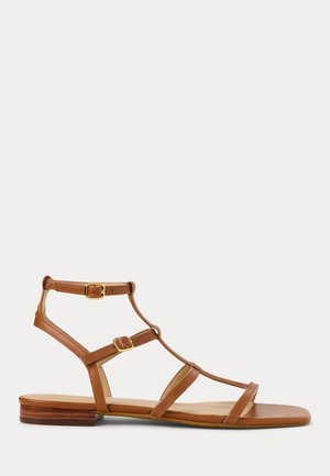 Sandalias gladiadoras de cuero marrón con correas en los tobillos y hardware dorado. Suela plana, diseño de punta abierta, con múltiples correas finas para mayor sujeción.