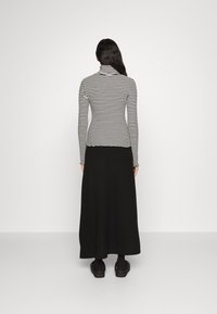 Zwarte lange rok gecombineerd met een aansluitende zwart-wit gestreepte coltrui. Glad stof met een minimalistisch ontwerp, gezien vanaf de achterkant.