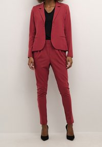 Blazer bordeaux à bouton unique, associé à un pantalon fuselé assorti. Texture lisse, coupe slim, et porté avec des escarpins noirs.