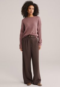 Geribbelde, mauve gebreide trui gecombineerd met losse, hooggetailleerde bruine broek. Voorzien van een zwarte riem en neutralkleurige instapschoenen.