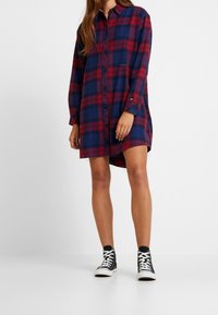 Röd och marinblå rutigt skjortklänning i bomull, med knapplist framtill, lång ärm och fickor, i kombination med svarta högskor.