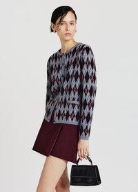 Grau gestrickte Strickjacke mit Rautenmuster in Burgunderrot und Schwarz, mit Knöpfen und figurbetonter Silhouette. Kombiniert mit einem bordeauxroten Rock.