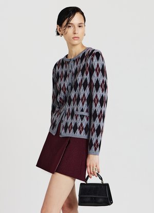 Grau gestrickte Strickjacke mit Rautenmuster in Burgunderrot und Schwarz, mit Knöpfen und figurbetonter Silhouette. Kombiniert mit einem bordeauxroten Rock.