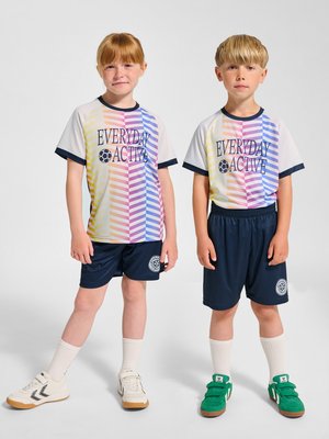 To børn står side om side iført matchende sportstrøjer med flerfarvede striber og marineblå shorts med hvide sokker og sneakers.