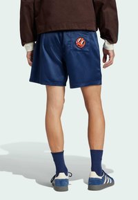 Marinblå satinshorts med en cirkulär grafisk design i röd och orange på bakfickan. Stylat med blå sneakers och blå ribbade strumpor.